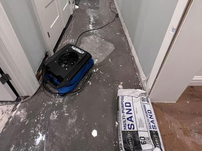 Floor fan drying water damaged hallway with sandbag.